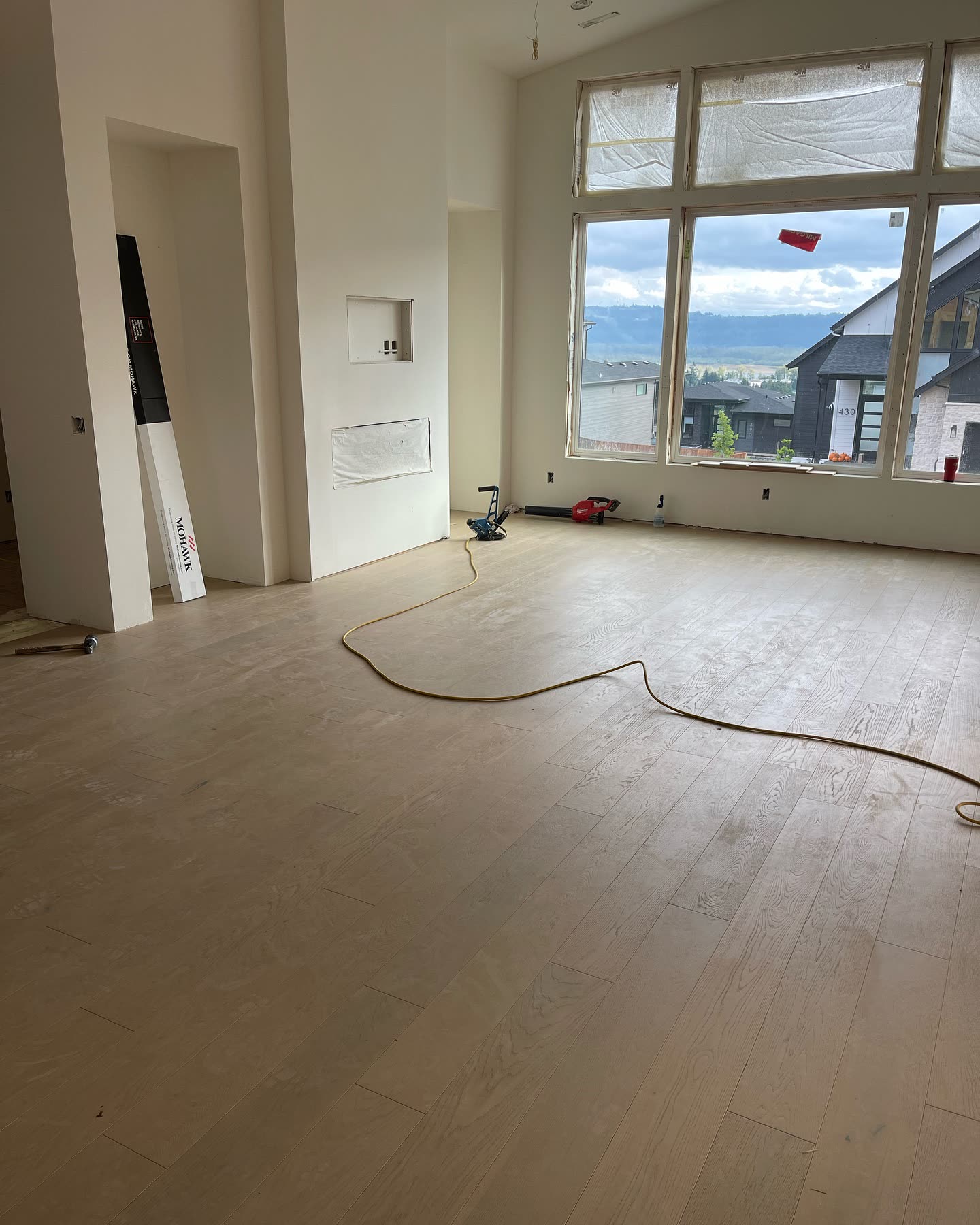 A vaulted great room in a Portland-area custom home, wide-plank oak floor running out to a wall of windows over the valley