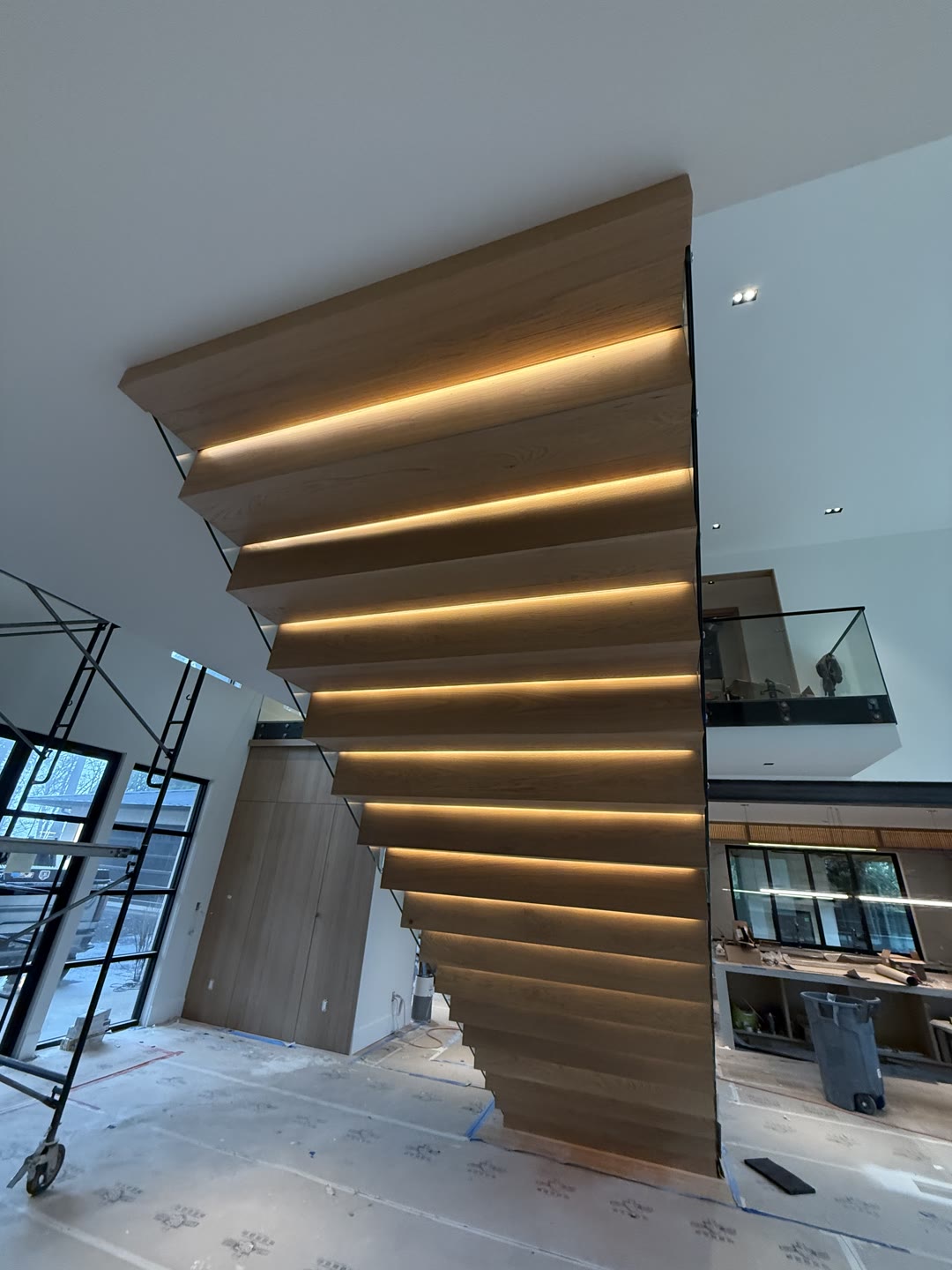 A floating staircase of thick white-oak treads cantilevered from a central steel spine, with LED underlighting and a glass-railed landing above