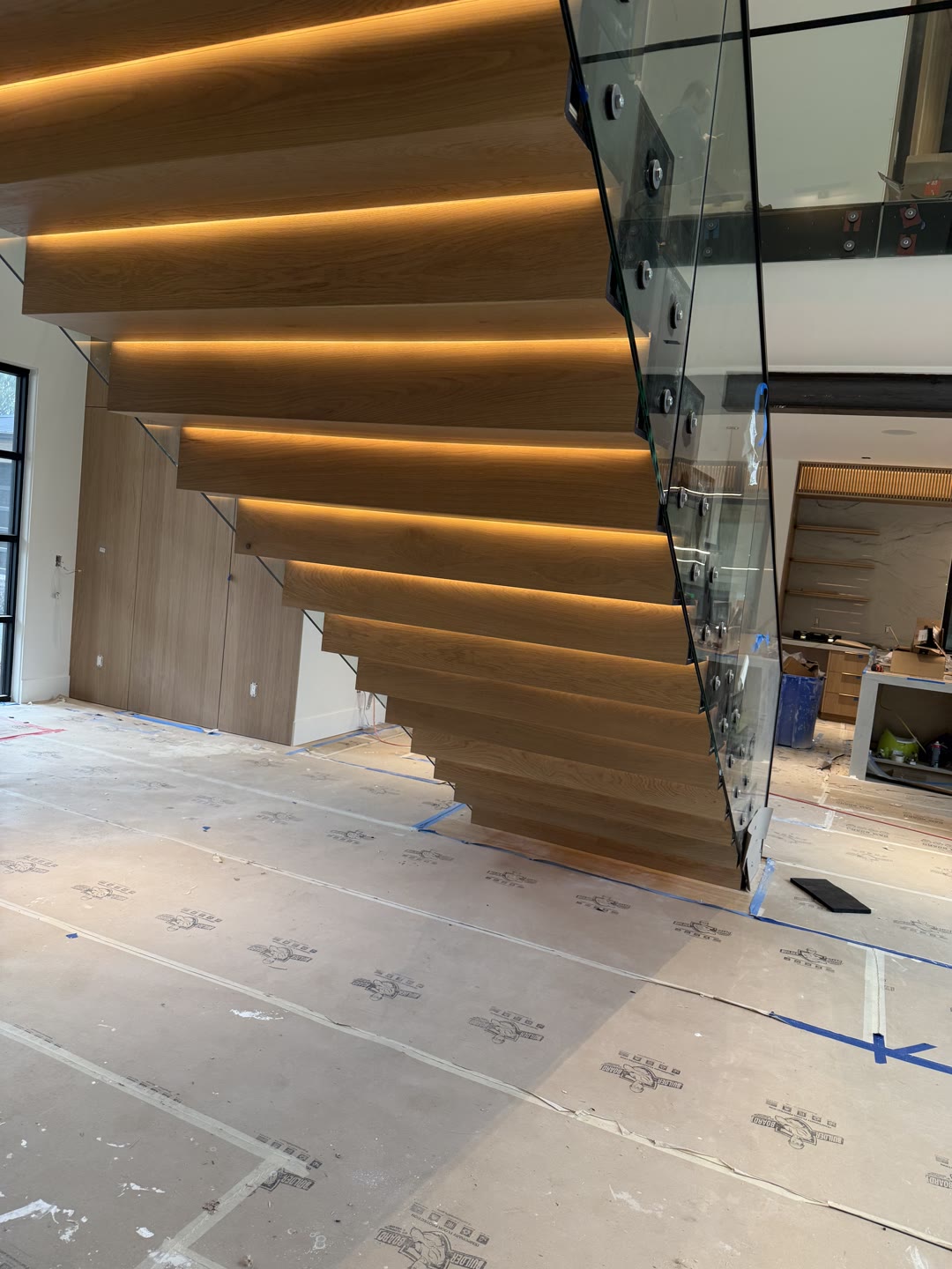 A floating white-oak staircase with LED-lit treads and a glass rail, cantilevered from a steel spine in a custom home by Grand Com