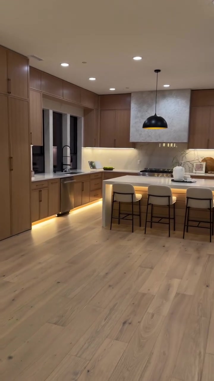 Wide-plank hardwood floor through a finished kitchen with island and pendant lighting